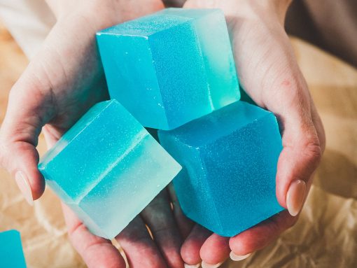 Small squares of bright blue soap being held out in hands.