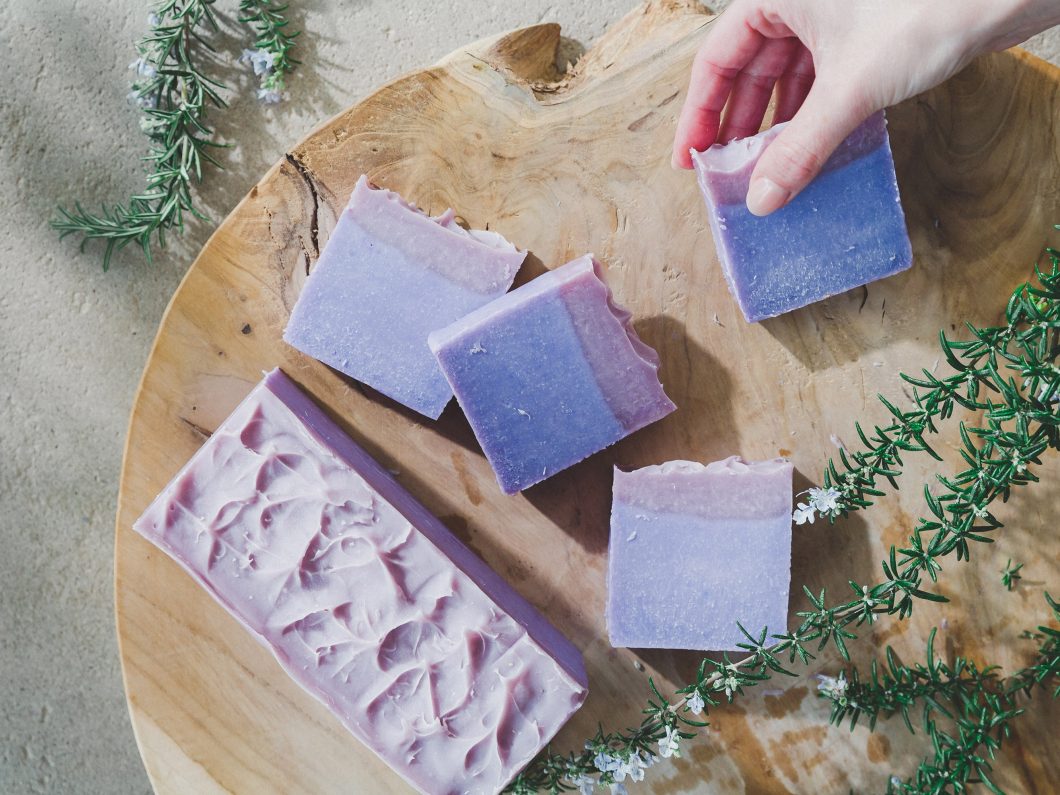 Lavender soap bars laid out on a round wooden board with rosemary on the side.