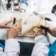 Two people in white coats and blue aprons cutting up a block of solid soap.